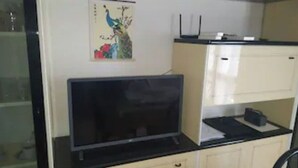 Une pièce avec un téléviseur à écran plat posé sur un meuble noir, un petit meuble avec un plateau noir et un routeur fixé au mur.