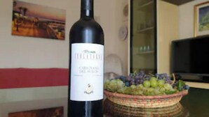 Une bouteille de vin sur une table, avec un panier de raisins en arrière-plan.