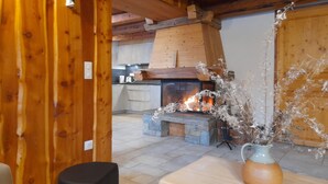 A rustic interior with a stone fireplace, wooden beams, and a kitchen area.