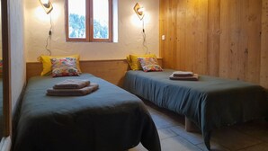 A room with two beds, wooden walls, a window, and wall-mounted lights.