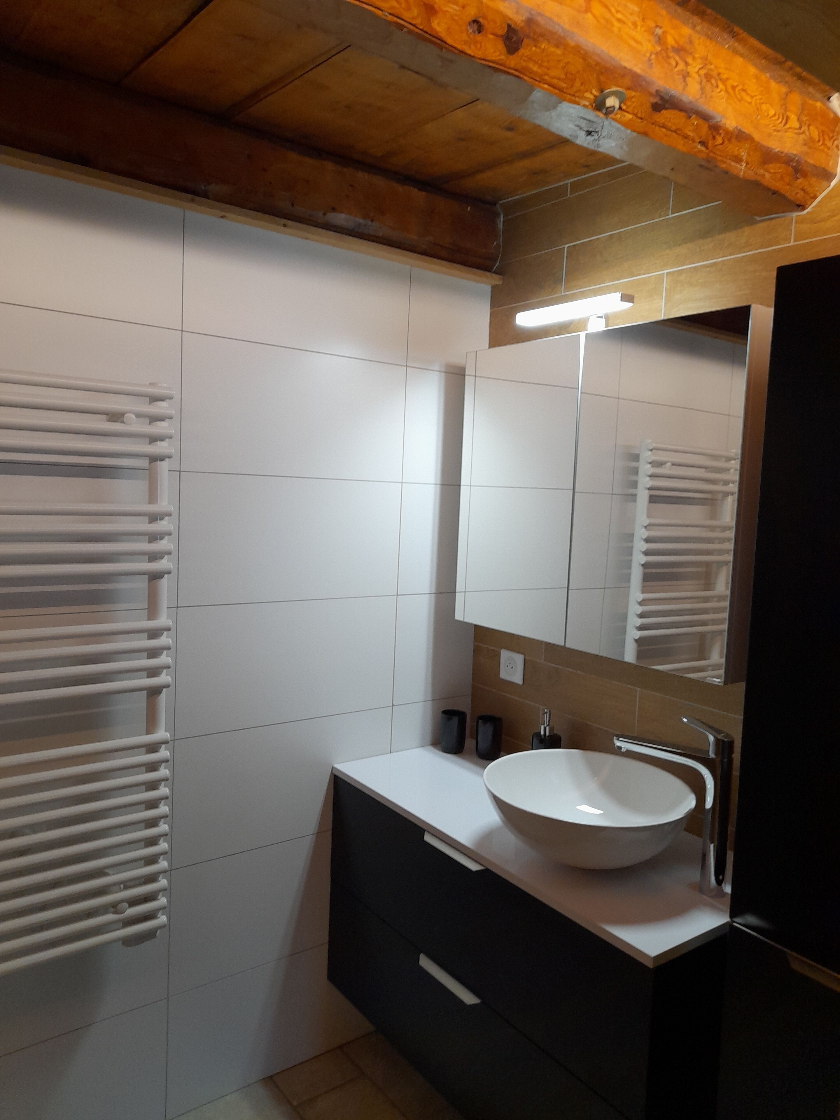 A modern bathroom with white tiled walls, a wooden ceiling, a white sink, and a mirror.