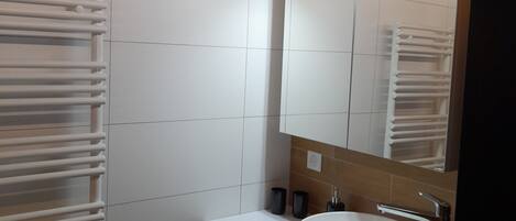 A modern bathroom with white tiled walls, a wooden ceiling, a white sink, and a mirror.