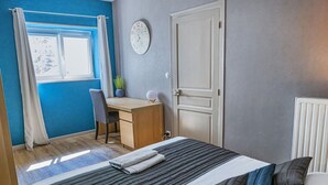 Ein Schlafzimmer mit Bett, Schreibtisch, Stuhl, einer Uhr und einem Heizkörper.