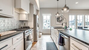 Une cuisine moderne dotée d’un îlot central, d’appareils électroménagers en acier inoxydable et de luminaires suspendus.