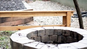 Un banc en bois et un foyer circulaire en pierre, le tout installé à l’extérieur.