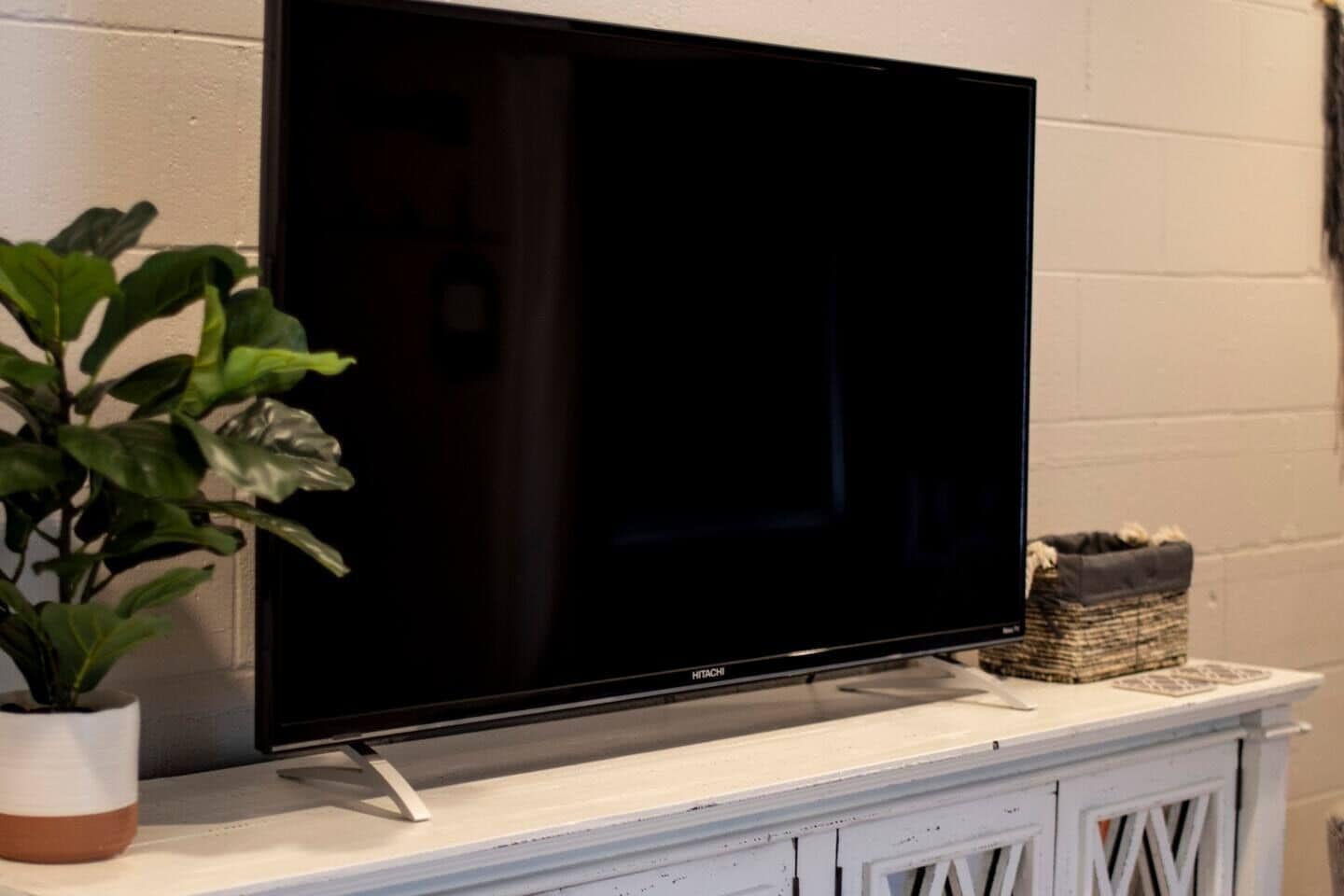 A flat-screen TV on a white cabinet with a plant beside it.