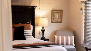 Une chambre à coucher bien rangée, avec un grand lit, une table de chevet avec une lampe, une chaise et un tableau encadré au mur.