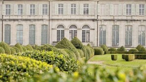 A classical building with symmetrical architecture, manicured gardens, and a formal lawn.