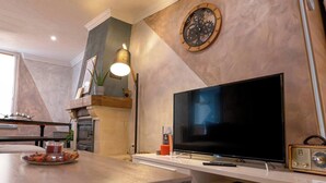 A modern kitchen with a flat-screen TV, a wooden dining table, and a decorative wall clock.