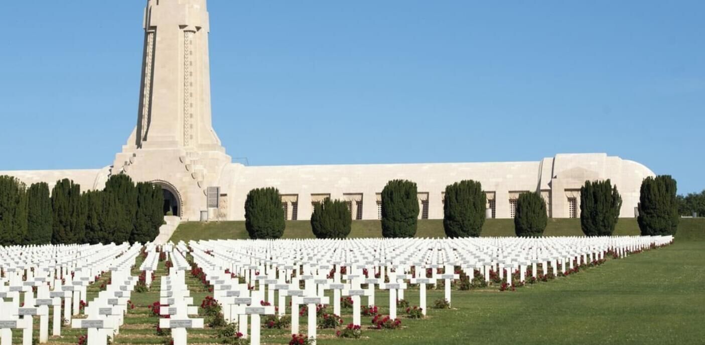 Un edificio grande con una torre alta y hileras de lápidas blancas en un cementerio.