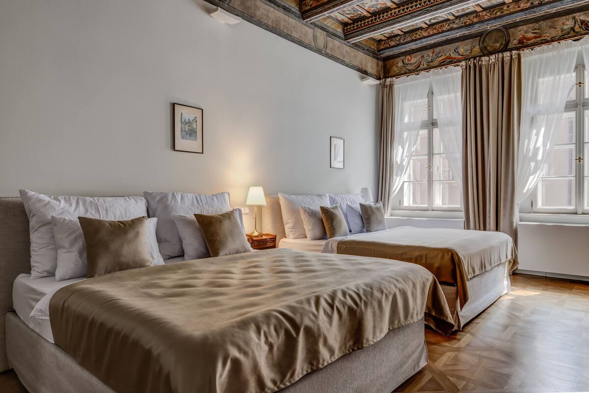 A hotel room with two beds, a nightstand, a lamp, and a large window with curtains.