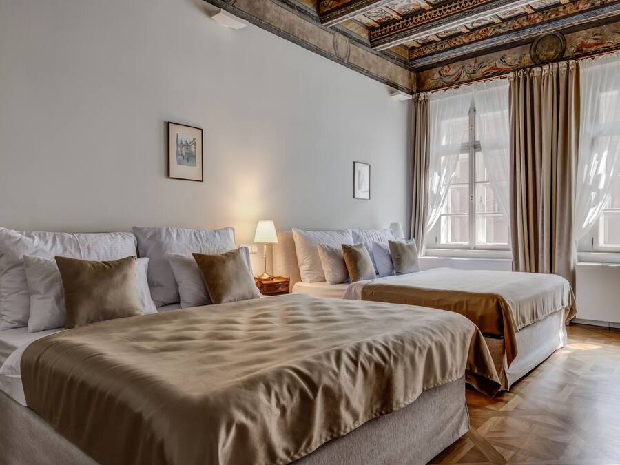 A hotel room with two beds, a nightstand, a lamp, and a large window with curtains.