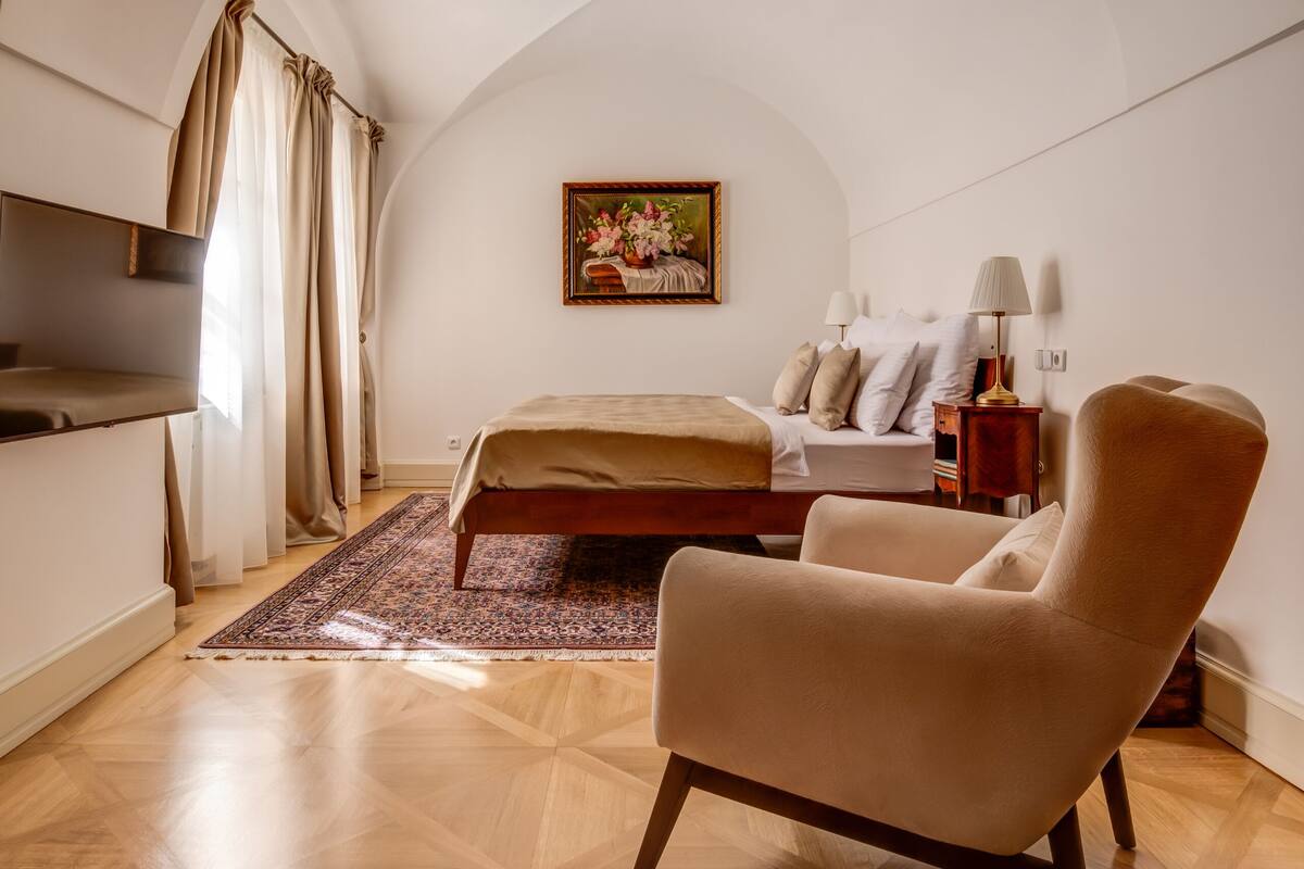 A bedroom with a bed, a chair, a TV, and a painting on the wall.