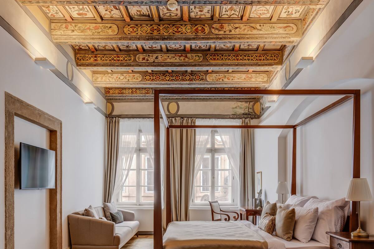 A four-poster bed with a wooden frame, a sofa, and a television mounted on the wall.