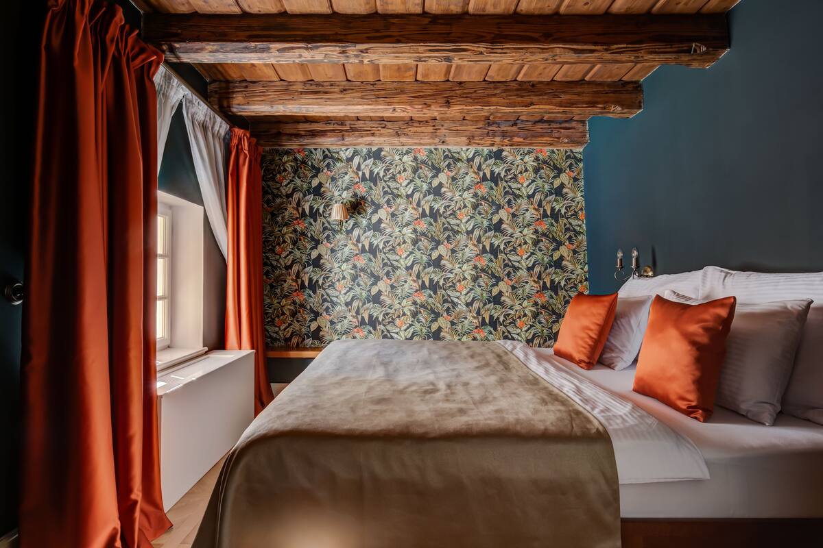 A bedroom with a wooden ceiling, a floral wallpaper, and a bed with orange pillows.
