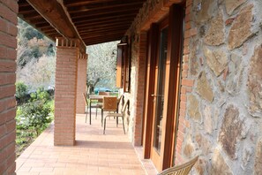 Un patio couvert doté d’un sol en briques, de murs en pierre et d’un espace détente avec des chaises et une table.