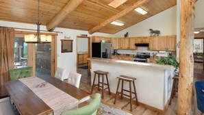 Cozinha espaçosa com armários de madeira, uma ilha central e um espaço de refeições com uma cadeira verde.