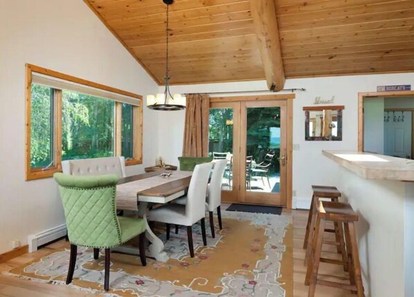 A dining area with a wooden ceiling, large windows, and a view of the outdoors.