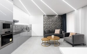 A modern kitchen with built-in appliances, a dining area with two round tables, and a seating area with a sofa and cushions.