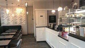 A restaurant with a long counter, hanging pendant lights, and a display case with baked goods. - Avand Apartments Debrecen (Debrecen)