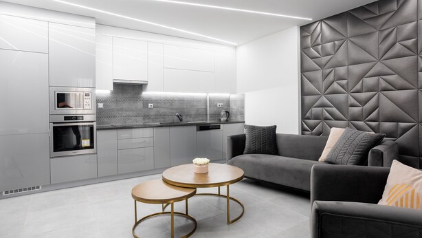 A modern kitchen with built-in appliances, a grey sofa, and a decorative wall panel. - Avand Apartments Debrecen (Debrecen)