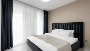 A modern hotel room with a large bed, dark curtains, and a neutral color scheme. - Avand Apartments Debrecen (Debrecen)