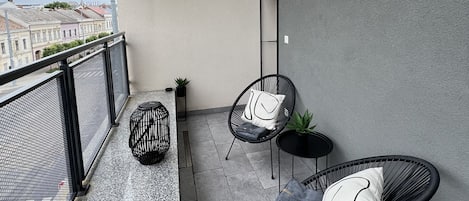 A balcony with two black wire-framed chairs, a small table, and a potted plant.