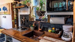 A kitchen with a wooden countertop, a sink, a microwave, and various kitchen utensils and plants. - Cozy AF Tiny-House Oasis (Tampa)