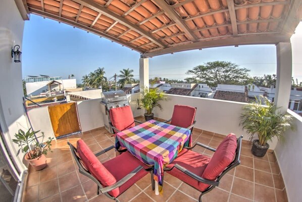 A covered outdoor patio with a table and chairs, a grill, and potted plants.