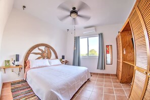 A bedroom with a bed, a ceiling fan, a window with curtains, and a wooden wardrobe.
