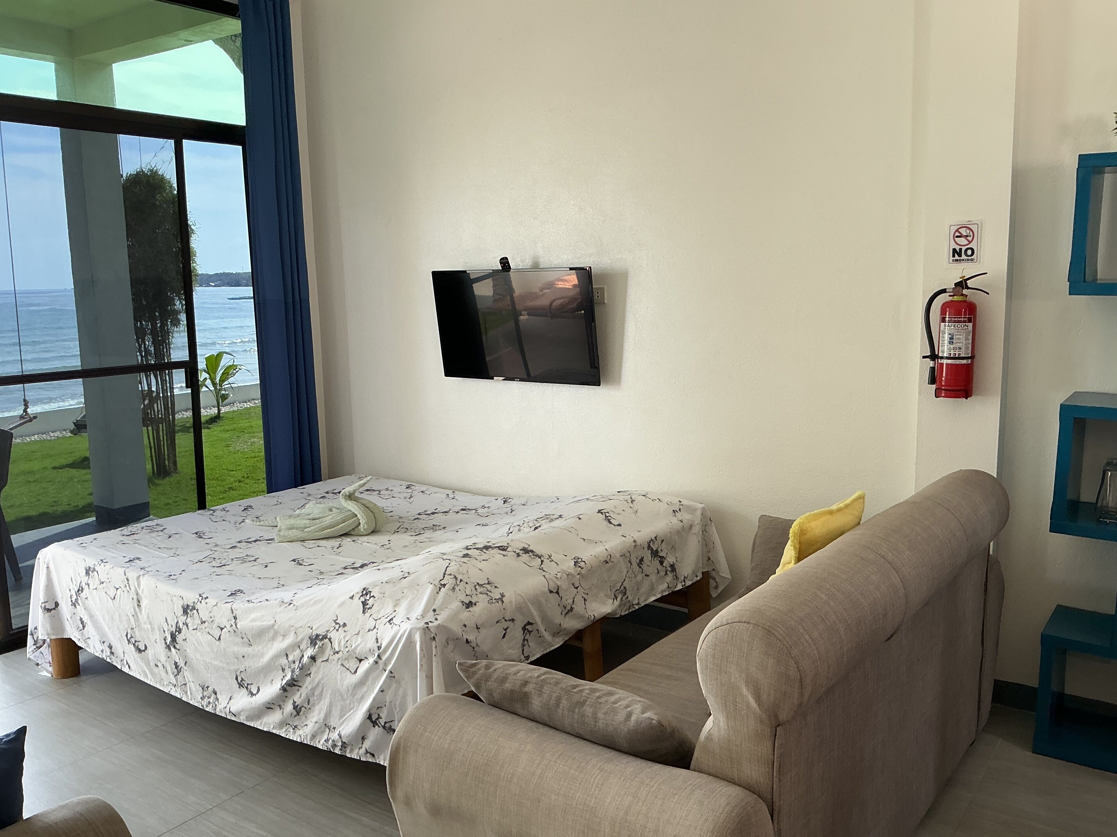 Een slaapkamer met een bed, een bank, een televisie en uitzicht op zee.