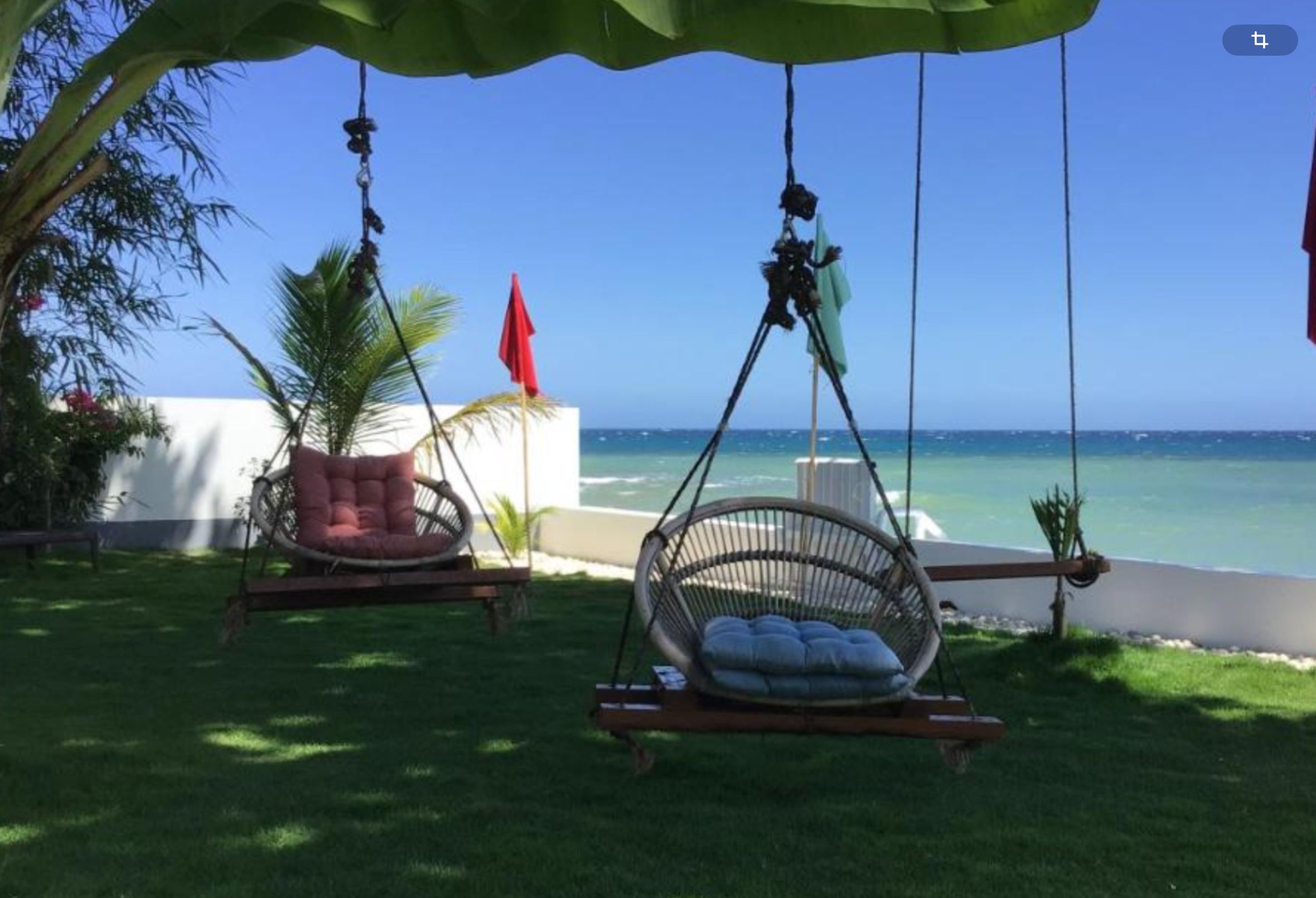 Two wicker swing chairs with cushions, a red flag, and a view of the ocean.