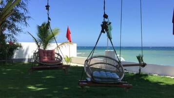 Two wicker swing chairs with cushions, a red flag, and a view of the ocean.