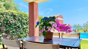 Patio esterno con tavolo e sedie, piscina e vista sul mare.