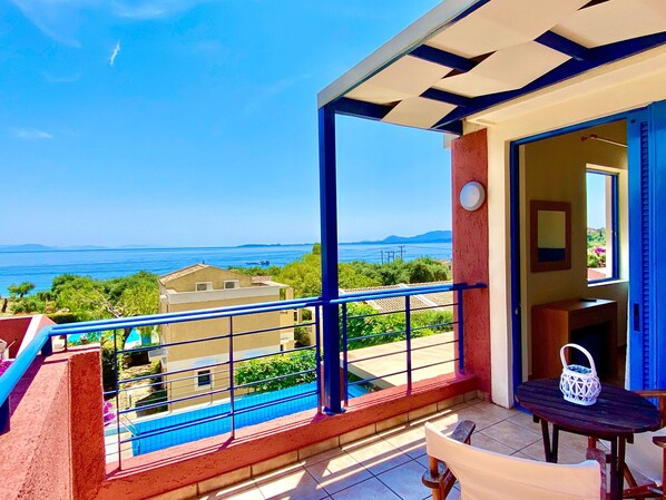 A balcony with a view of the sea, a pool, and a table with a lantern.