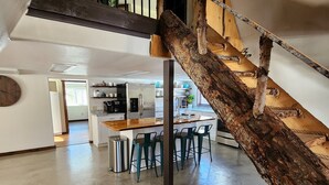 A spacious loft with a wooden staircase, a kitchen area, and a dining space.