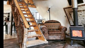 Een rustiek interieur met een houten trap, een bank, een open haard en een plafondventilator.