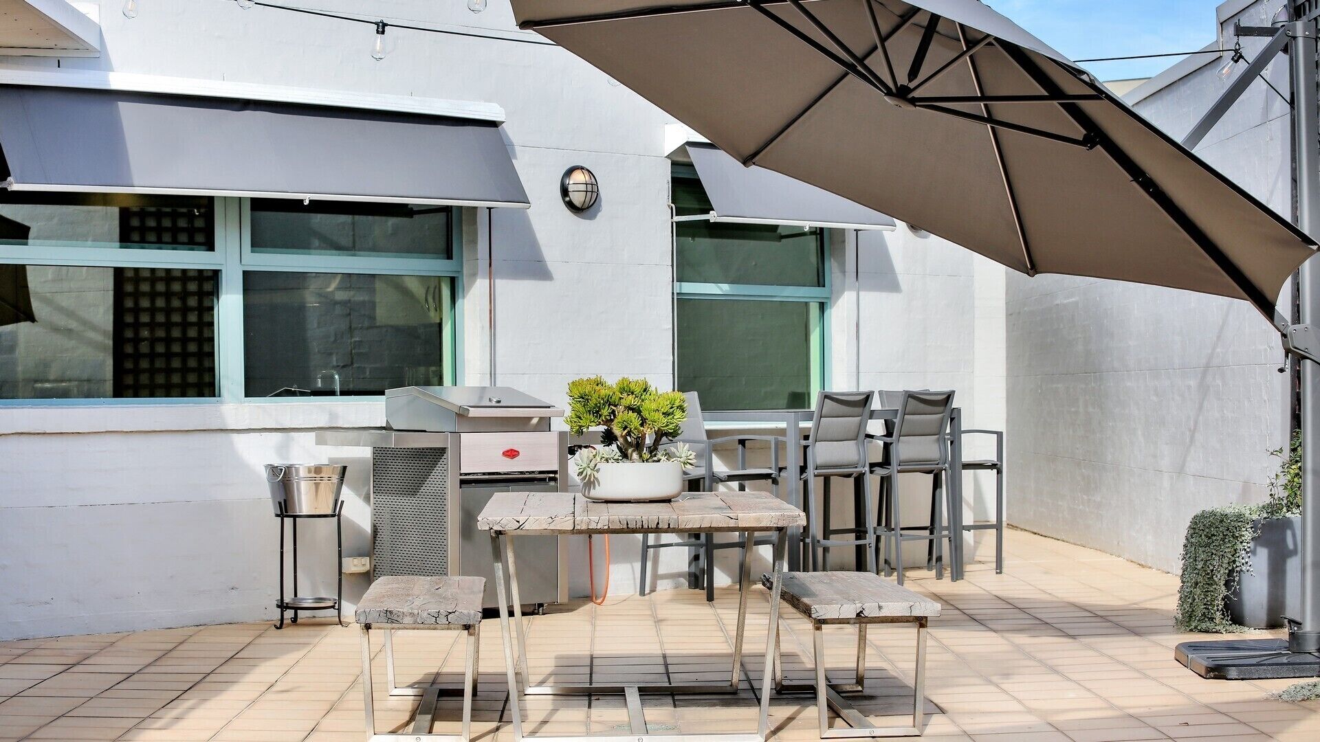 An outdoor patio with a grill, seating, and a potted plant.