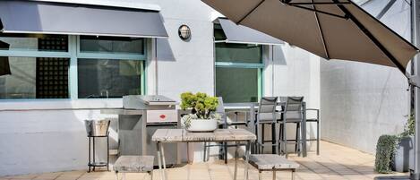 An outdoor patio with a grill, seating, and a potted plant.