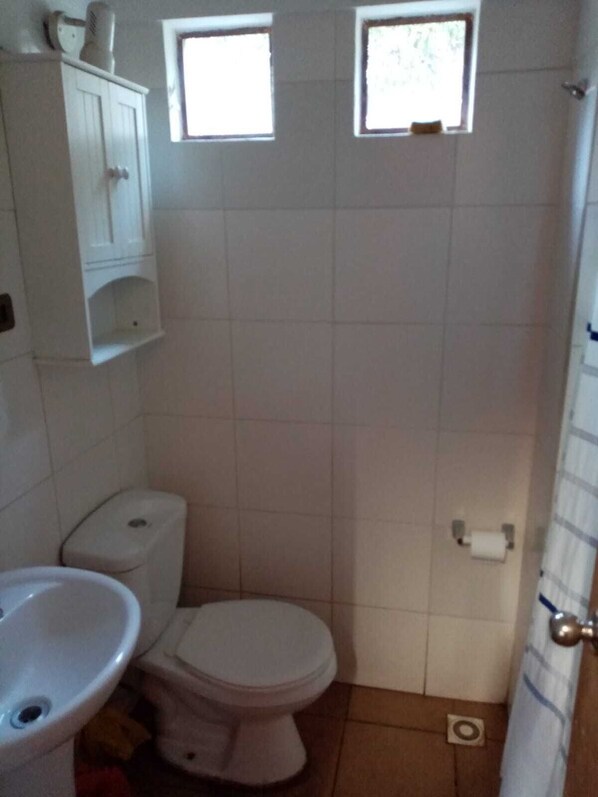 A small, clean bathroom with a toilet, sink, and two windows. - casa olmue con piscina (Olmue)