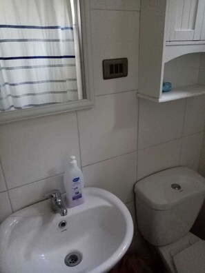 Un baño con un lavamanos blanco, un inodoro y una ventana con cortina a rayas.