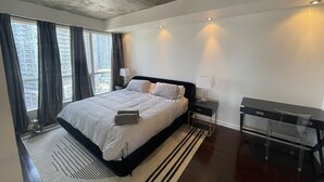 A modern hotel room with a large bed, bedside tables, a desk, and a view of the cityscape through the window. - Spectacular Terrace - City/Lake View - 5 mins from major attractions (Toronto)