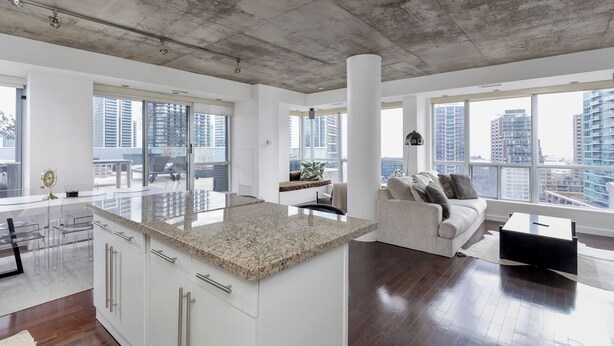 A spacious living area with a large window, a white sofa, and a kitchen island. - Spectacular Terrace - City/Lake View - 5 mins from major attractions (Toronto)