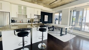 A modern kitchen with white cabinetry, a central island with bar stools, and a large window providing a view of the outdoors. - Spectacular Terrace - City/Lake View - 5 mins from major attractions (Toronto)