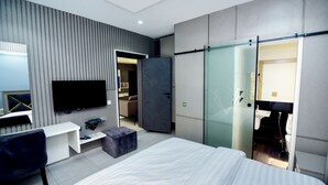 Una habitación de hotel moderna con una cama grande, televisión de pantalla plana, escritorio y puerta corredera al baño.