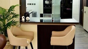 Una cocina moderna con una isla central, dos taburetes de bar, iluminación colgante y una planta en maceta.