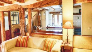 Een gezellige kamer met zichtbare houten balken, een bank met gestreepte kussens en een lamp op een bijzettafeltje.