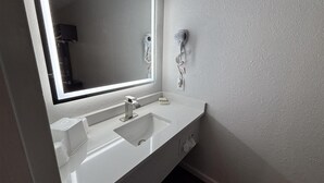 A bathroom with a white sink, a mirror with a light, and a hairdryer mounted on the wall. - Motel 6 – Conway, SC (Conway)