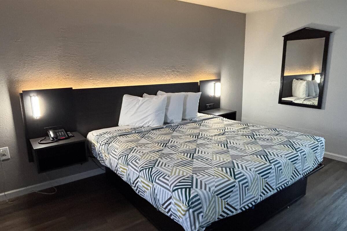 Une chambre d’hôtel moderne avec un grand lit, une table de chevet, une lampe de chevet et un miroir au mur.