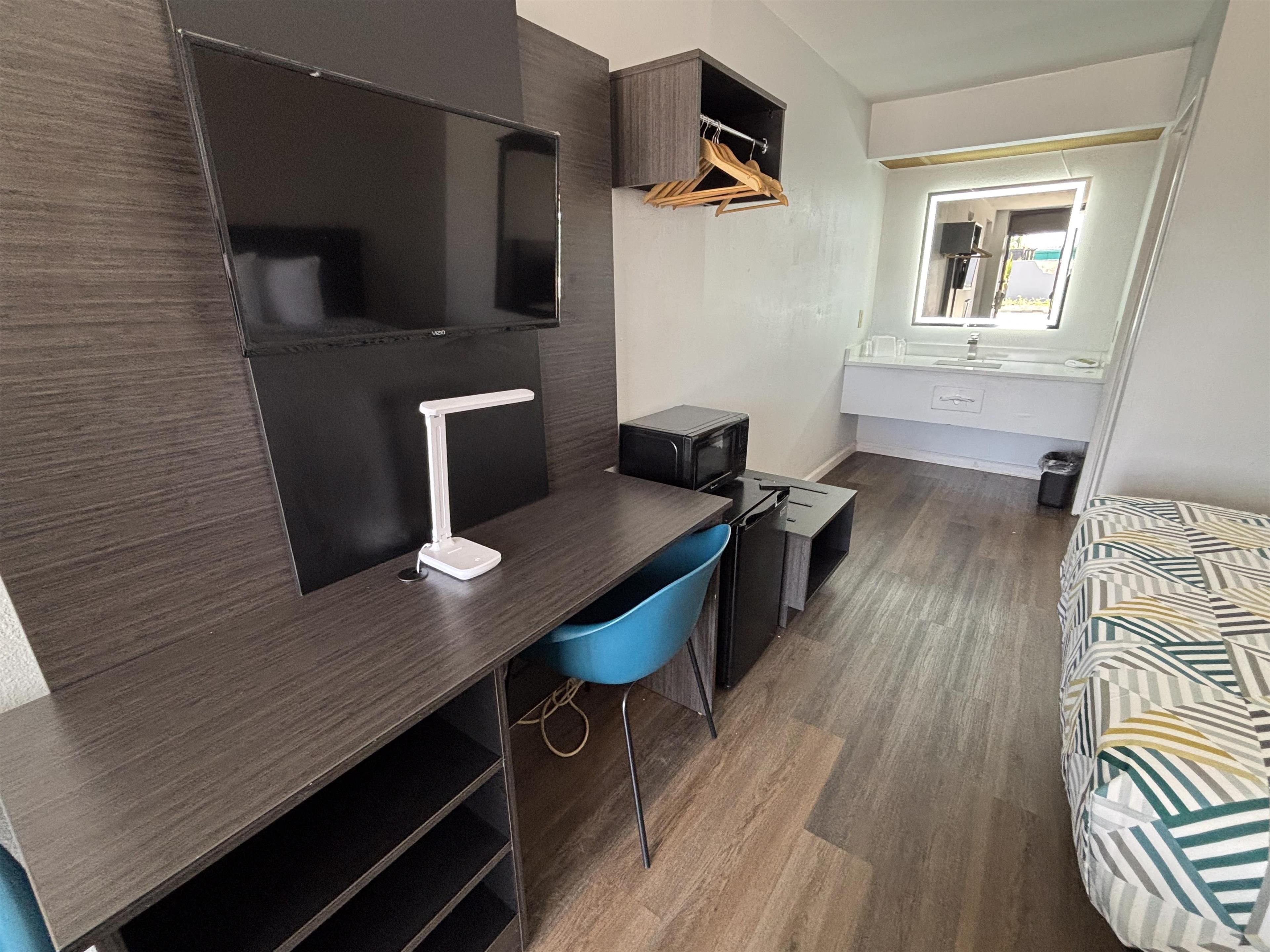 Une pièce compacte comprenant un bureau, une chaise, un lit, un téléviseur et une petite kitchenette.